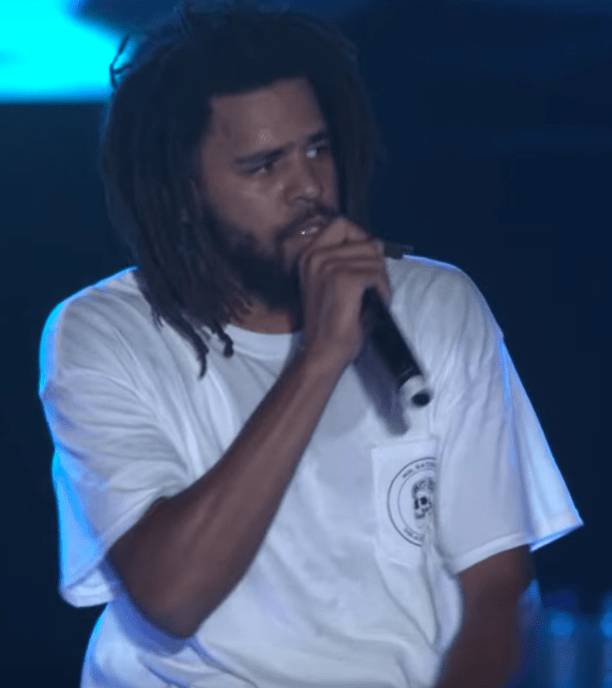 J. Cole with mic in hand, wearing a white t-shirt.