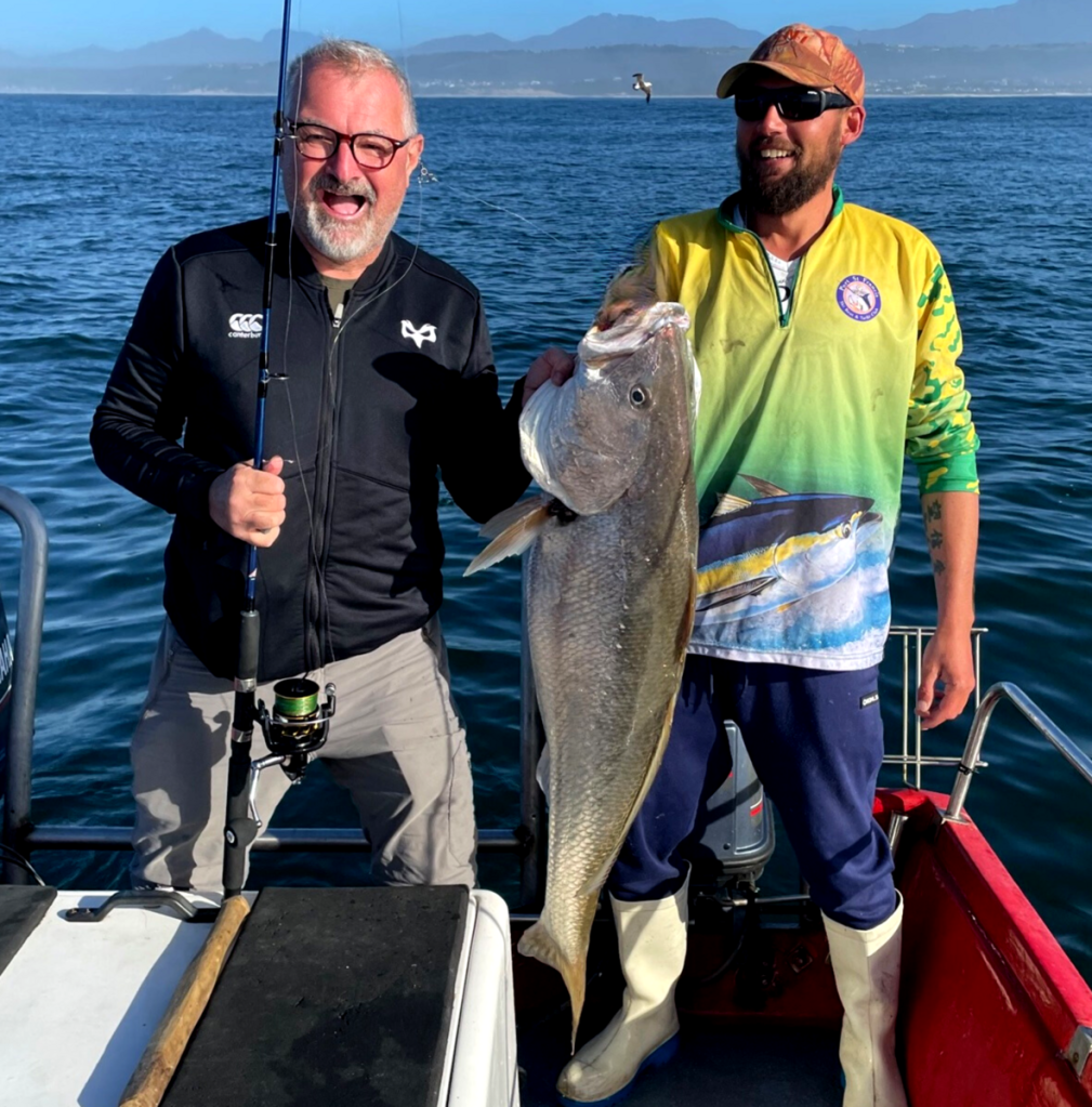 Two men on fishing boat holding a caught fish.
